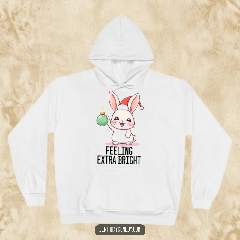 Funny Rabbit Holiday Hoodie: A joyful rabbit sporting a festive hat holds a shiny ornament high, embodying holiday excitement.