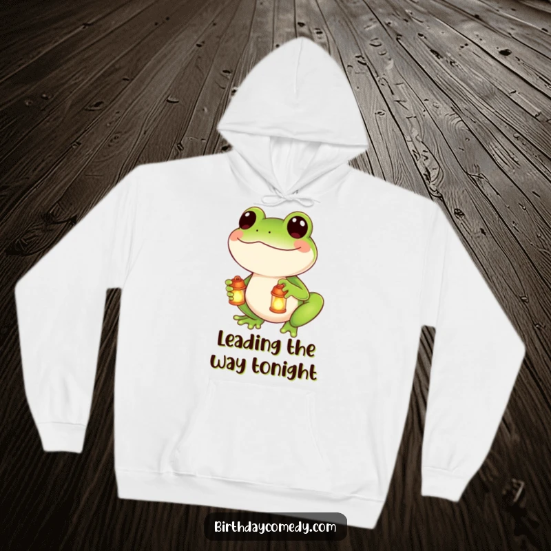 Funny hoodie with a smiling frog character holding a miniature glowing lantern, offering comfort and a touch of enchantment.